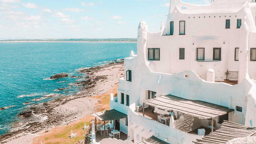 Casapueblo, the iconic sculptural building in Punta del Este, Uruguay, perched on rocky coastline with expansive views of the blue sea, under clear skies.