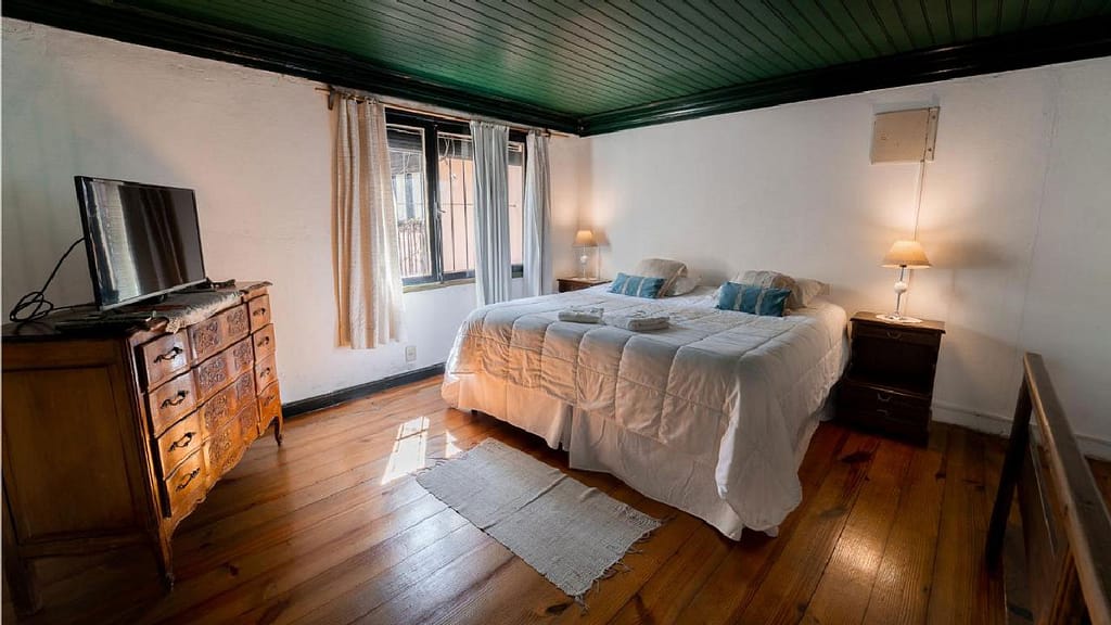 A modest room at Posada de la Flor in Colonia del Sacramento, characterized by antique furniture and a bed with white sheets.