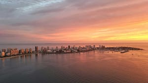 Aerial view of Punta del Este, Uruguay, at sunset with the skyline silhouetted against a pastel-colored sky, reflecting over the calm sea waters.