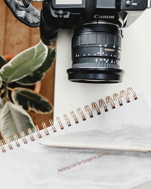A close-up of a Canon camera and a weekly planner with a white pen on a marbled surface, embodying essential gadgets and electronics to bring along for productive and creative endeavors.