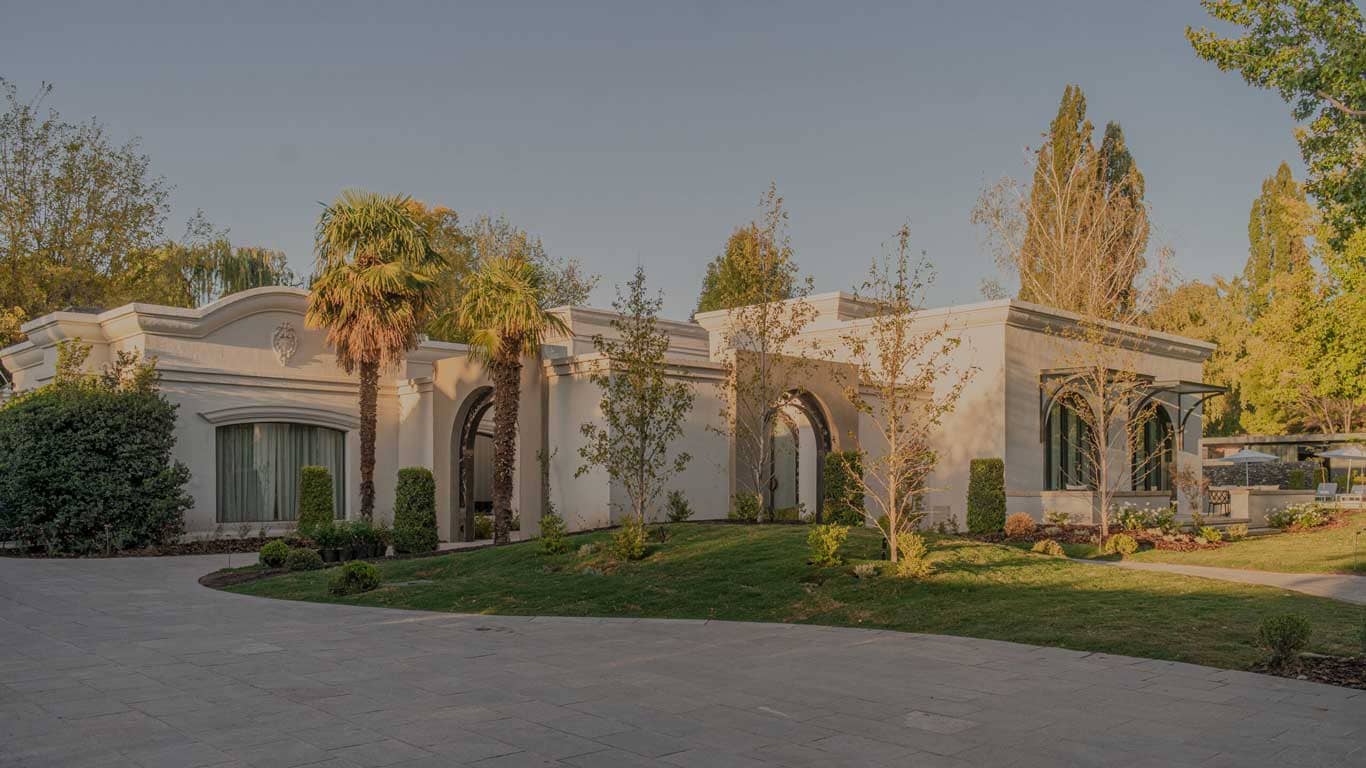 The luxurious Susana Balbo hotel in Chacras de Coria, Mendoza, bathed in the warm glow of sunset, showcasing elegant architecture with palm trees and lush gardens, inviting a peaceful and exclusive stay in the wine region.