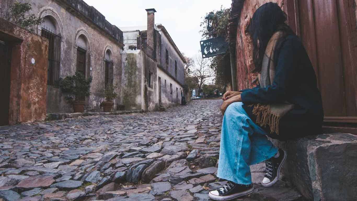 Woman sitting on the curb of the cobblestone streets in the old town of Colonia del Sacramento.