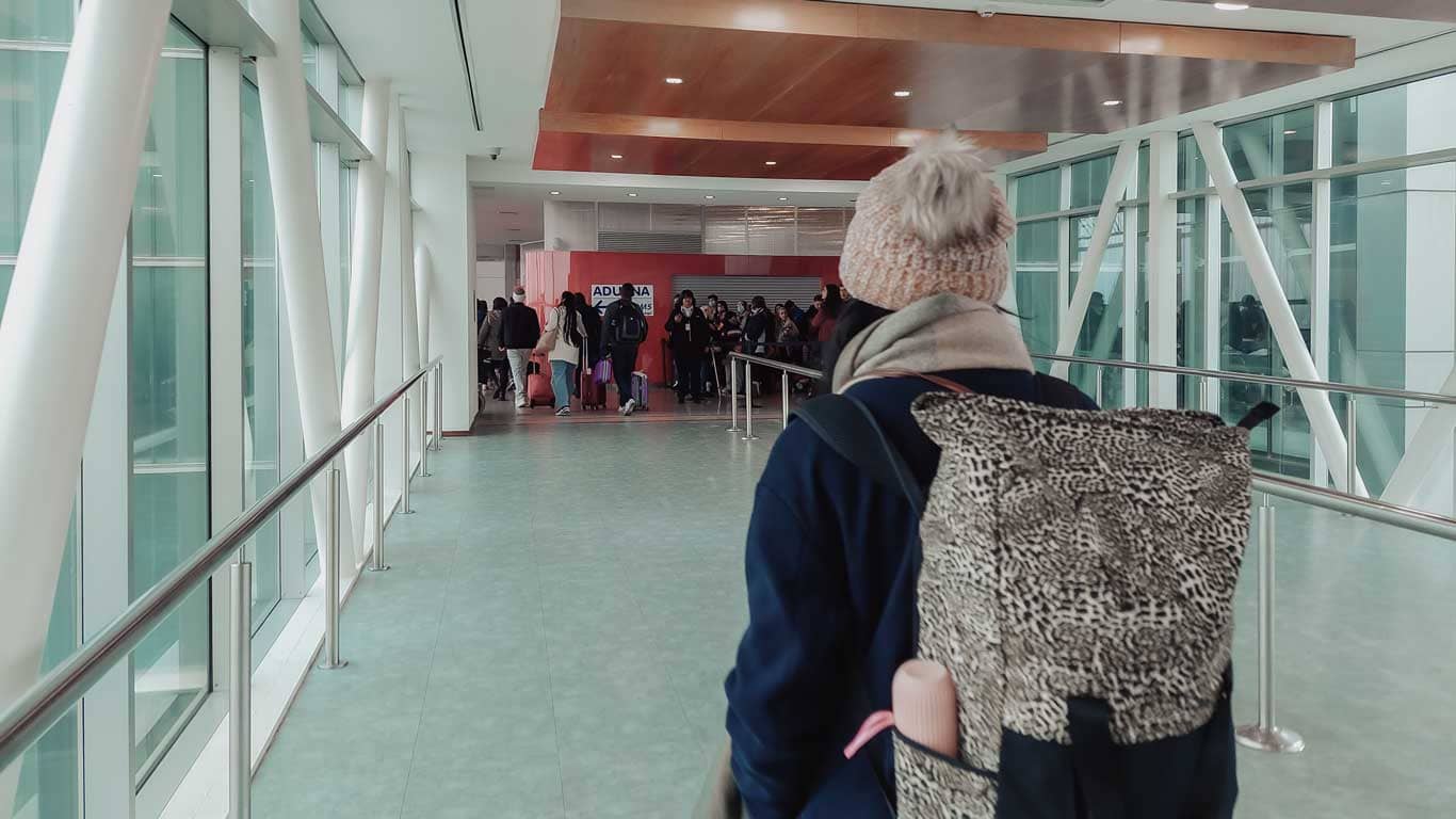 A woman wearing a beanie and a windbreaker jacket, with a backpack on her back, walking down the corridor to board the Buquebus ferry.