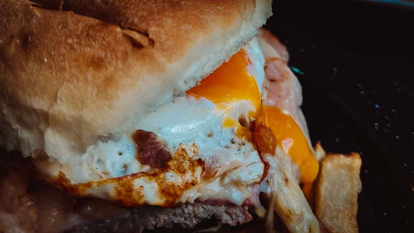 Image of the typical Uruguayan sandwich, the chivito, where the egg yolk delicately runs over the other ingredients, enhancing the appetizing combination of flavors.