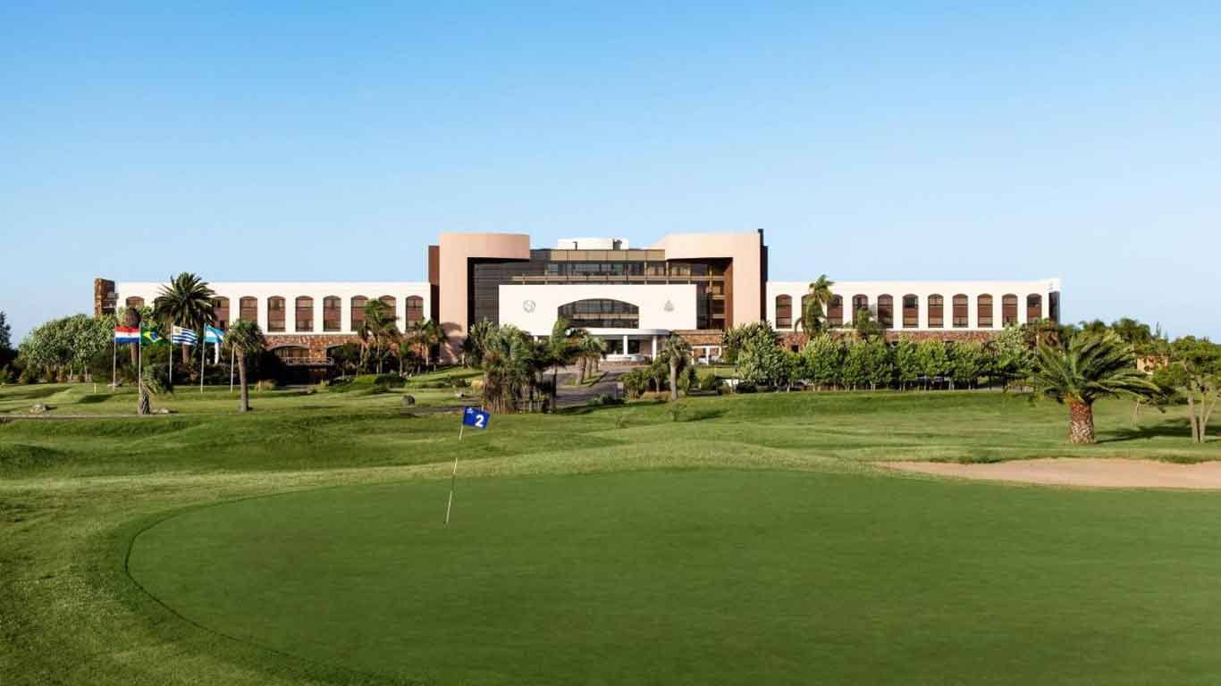 The imposing structure of the Sheraton Colonia Golf & Spa Resort is portrayed, standing out, with its golf course in the foreground.