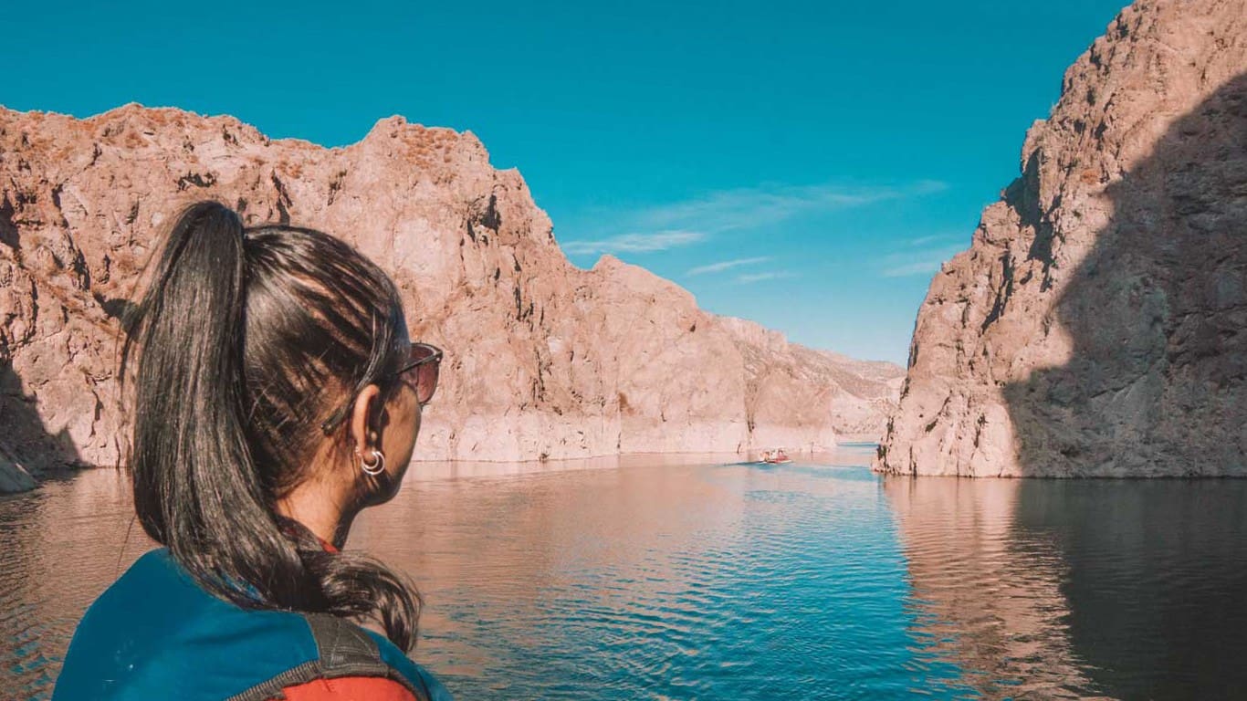 A woman with a ponytail looking out over the serene, blue waters of Cañon del Atuel in Mendoza in january, with rugged cliffs under a clear sky in the background.