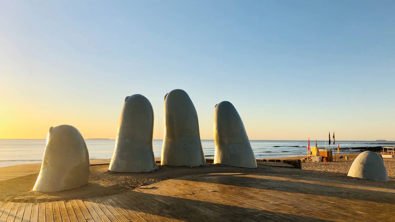 The 'La Mano' sculpture, known as 'Los Dedos,' shows five giant fingers emerging from the sand at Brava Beach in Punta del Este, captured at dawn with the serene ocean horizon in the background.