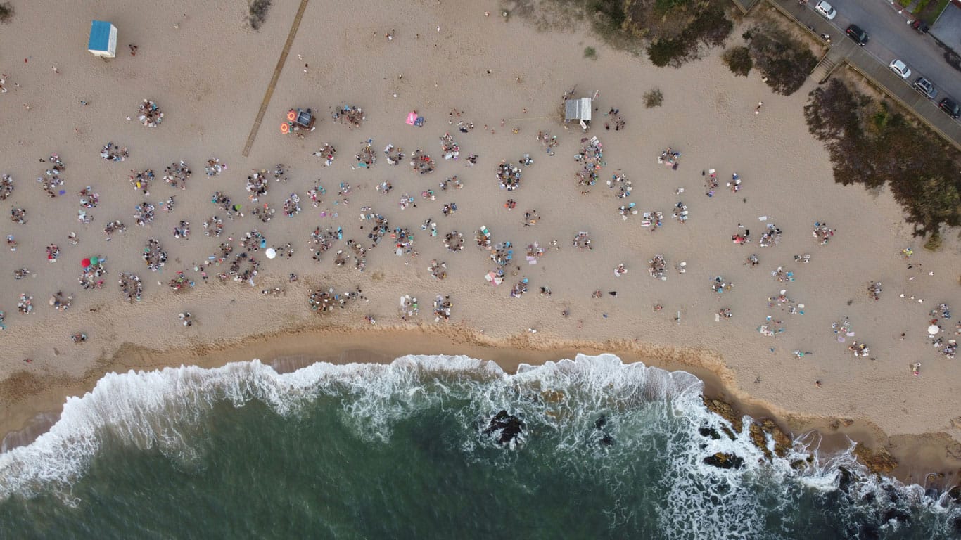 Overhead view of a crowded Manantiales beach in Punta del Este, with beachgoers scattered on the sand, umbrellas dotting the shoreline, and the dynamic white foam of the waves meeting the beach.